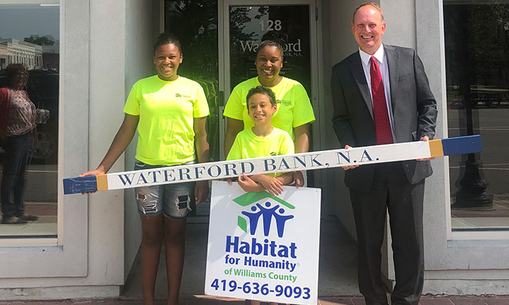 Community outreach - Male banker stands with habitat for humanity team holding a branded stud to be place in a new home.