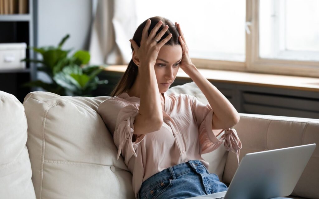A young woman looks frustrated while using buy now pay later services on her laptop.