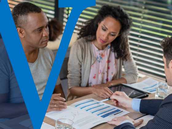 A banker presents charts to a couple during a meeting, symbolizing wealth planning for high-net-worth families. The couple listens attentively, reviewing printed documents, with a bold blue "W" watermark overlaying the image.